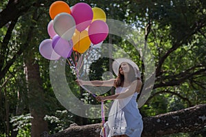 Young teen girl sitting on tree and holding balloons in hand.