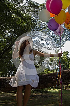 Young teen girl sitting on tree and holding balloons in hand.