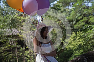 Young teen girl sitting on tree and holding balloons in hand.