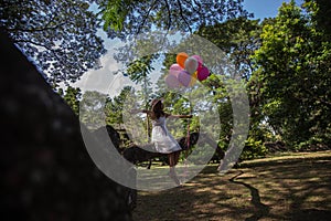 Young teen girl sitting on tree and holding balloons in hand.