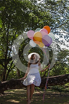 Young teen girl sitting on tree and holding balloons in hand.