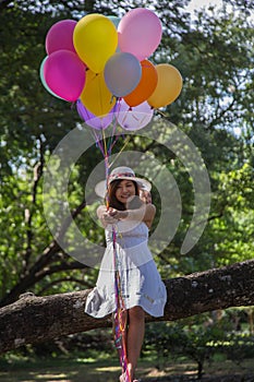 Young teen girl sitting on tree and holding balloons in hand.