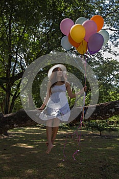 Young teen girl sitting on tree and holding balloons in hand.