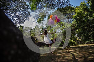 Young teen girl sitting on tree and holding balloons in hand.