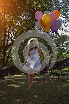 Young teen girl sitting on tree and holding balloons in hand.