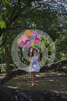 Young teen girl sitting on tree and holding balloons in hand.