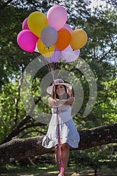 Young teen girl sitting on tree and holding balloons in hand.