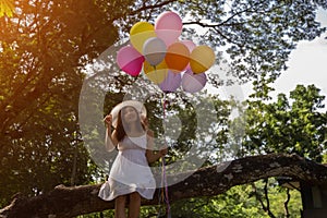 Young teen girl sitting on tree and holding balloons in hand.