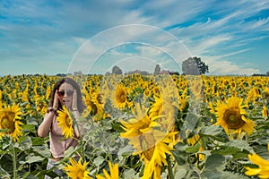 Young teen girl standing in field surrounded by sunflowers wearing sunglasses