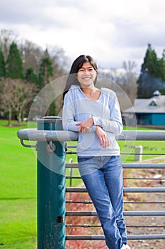 Young teen girl standing, leaning against railing at park