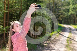 Young teen girl traveler taking selfie on mobile phone in a summer day forest. girl looking at smartphone camera