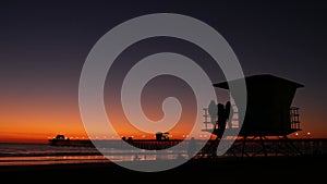 Young teen girls silhouettes, lifeguard watch tower, friends on pacific ocean beach, California USA.