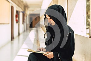 Young teen muslim niqab woman reading the Quran and faith The Holy Al Quran in University building. Arab black chador lady