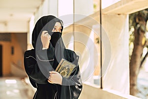 Young teen muslim niqab woman reading the Quran and faith The Holy Al Quran in University building. Arab black chador lady