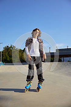 Young teen in rollerblades making stunt on cement ramp in skate park