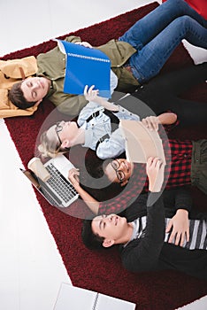young teen students lying on carpet with notebooks