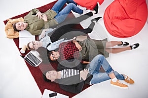 young teen students lying on carpet with notebooks