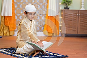Young teenagaer muslim boy reading Quran book during Ramadan feast celebration at home