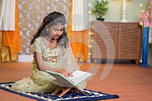 Young teenagaer muslim girl reading Quran book during Ramadan feast celebration at home