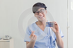 Young teenage Asian man holding credit card sitting on the bed in the hospital