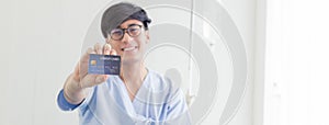 Young teenage Asian man holding credit card sitting on the bed in the hospital with smiley face. healthcare and medical concept