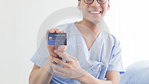 Young teenage Asian man holding credit card sitting on the bed in the hospital with smiley face. healthcare and medical concept