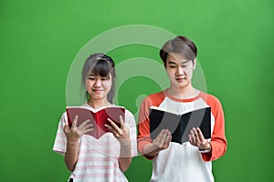 Young teenage boy and girl standing and reading at book at green