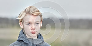 A young teenage boy looking sad and thoughtful while standing alone in a public park. Lonely child feels bad because he