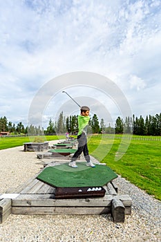 Young teenage boy outdoors at a driving range playing golf and practice his swing.