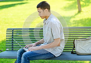 Young teenage boy using his laptop in the park