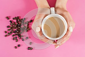 Woman hands holding cup of coffee and blurred coffee beans on pink desk