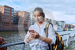 Young teenage female using smartphone outdoor, holding reading typing