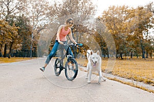 Young teenage girl on bicycle with white dog Husky on the road in the park