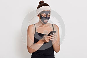 Young teenage girl with black face mask on her face using her smart phone, looking at device screen with astonished facial