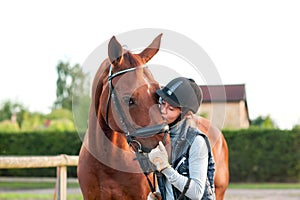 Young teenage girl equestrian kissing her chestnut horse.