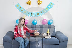 Young teenage girl having fun decorates the cake with candles in the shape of dog paws for her pet Jack Russell Terrier dog