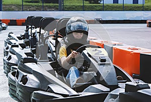 A young teenage girl in a helmet rides in a sports car on an open-air go-kart. Karting is a popular form of active recreation in m