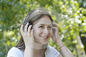 Young teenage girl listening music with headphones and smart phone in the park, summer portrait