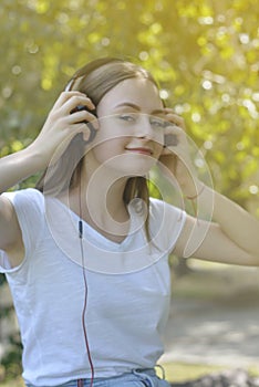 Young teenage girl listening music with headphones and smart phone in the park, summer portrait