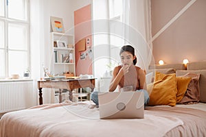 Young teenage girl looking at her latop and eating something.