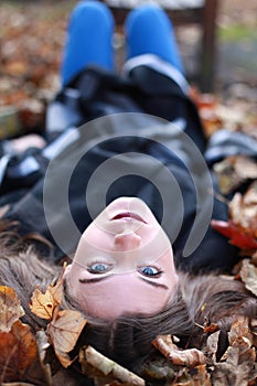 Young teenage girl lying upside down on a bed of leaves