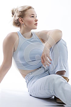 A young teenage girl sits and looks to the side. Cute blonde teenager with freckles on her face wearing a blue top and jeans.