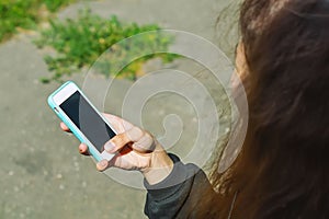 A young teenage girl is sitting outside on the street and holding a cell phone with a blank screen in her hands. Mobile phone in h