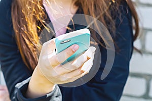 A young teenage girl is sitting outside on the street and holding a cell phone in her hands. Communication by Mobile phone. Love f