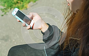 A young teenage girl is sitting outside on a Sunny day and holding a cell phone with a blank screen in her hands. Communication on
