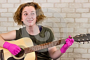 A young teenage girl smiles and plays the guitar in rubber gloves and learns chords or a song. Getting out of quarantine