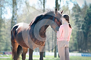 Young teenage girl standing with her favorite brown horse.