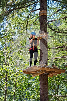 Young teenage girl standing on wooden board on tree trunk in forest adventure park