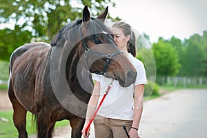 Young teenage girl tenderly kissing her favorite brown horse