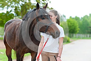 Young teenage girl tenderly kissing her favorite chestnut horse